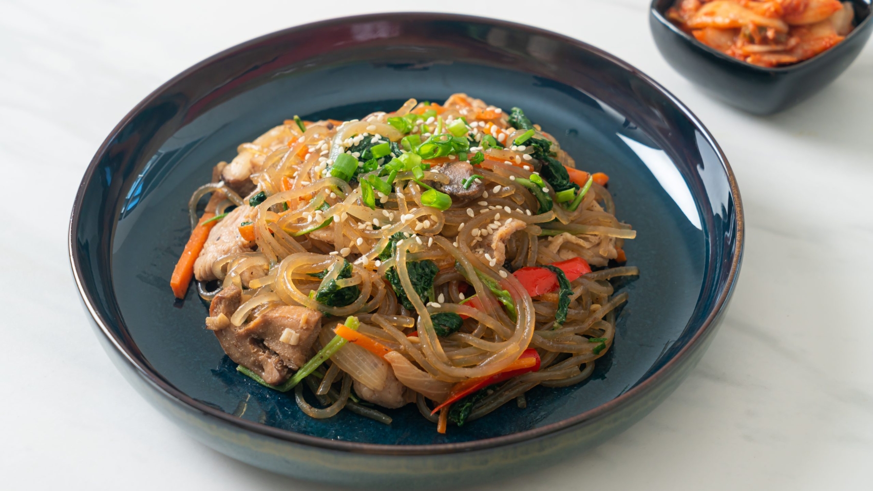 japchae or stir-fried Korean vermicelli noodles with vegetables and pork topped with white sesame - Korean traditional food style
